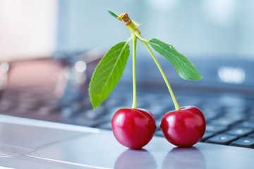 Red delicious cherry berries and glasses on a laptop_