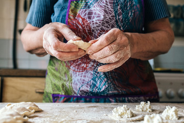 Preparing dumplings filled with cottage cheese. Elderly female hands making pierogi or pyrohy,...