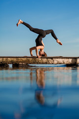 Young woman practicing yoga exercise at quiet wooden pier with city background. Sport and recreation in city rush