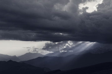 Silhouettes of cloudy mountains and sunbeams at summer evening