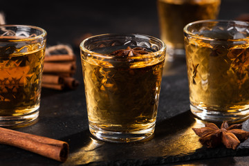 Shoot glass of alcoholic drinks with star anise and cinamon on metal table and black stone tray. 