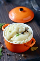 Dumplings with potatoes with herbs, spices and butter in a ceramic portion pot on a dark background. Varenyky, vareniki, pierogi, pyrohy - dumplings with filling.