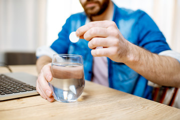 Man taking antipyretic or analgesic pills feeling bad while working on the laptop at home