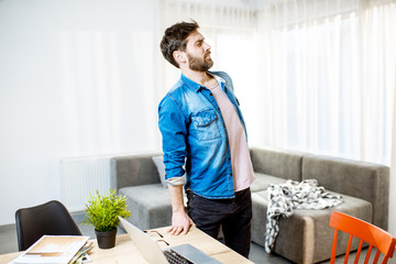 Man suffering from acute back pain while standing up from the working place at home