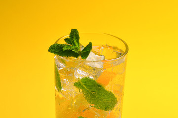 Cocktail with lemon and mint on a yellow background. Copy space.
