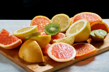 Sliced lemons, oranges, grapefruits and kiwi on a wooden plate.