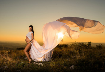 Pregnant beautiful white dressed girl standing on windy rock