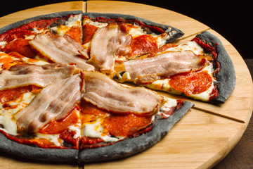 Pepperoni pizza with ham and sausages on black pastry.