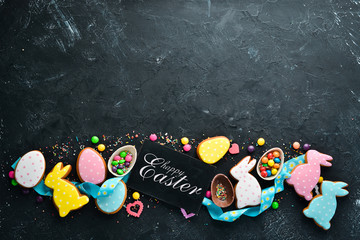 Easter greeting card. Happy Easter. Easter gingerbread cookies and decorative colored eggs. On a black background. Top view. Free copy space.