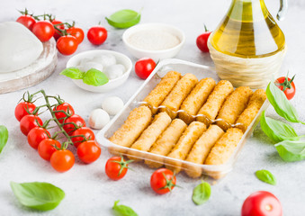 Fresh Mozzarella cheese on vintage chopping board with tomatoes and basil leaf with olive oil and tray with cheese sticks on stone kitchen table background.
