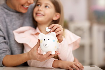 Young girl and her mother with piggybank sitting at table