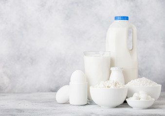Fresh dairy products on white table background. Plastic bottle and glass of milk, bowl of cottage cheese and baking flour and mozzarella. Eggs and cheese. Space for text