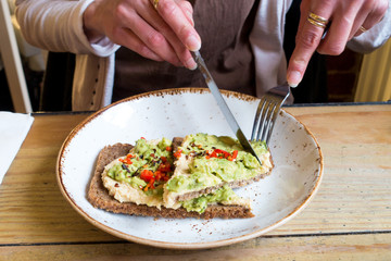 Woman eating a healthy lunch of avocado and hummus on rye toast, served in a wide white dish 