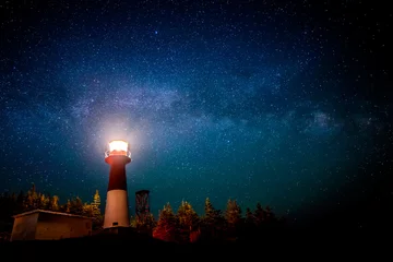  Een vuurtoren & 39 s nachts met een sterrenhemel erboven. Het licht in de bovenkant van de vuurtoren wordt verlicht. De Melkweg is zichtbaar. © madscinbca