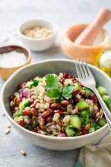 Healthy pearl barley salad with beans, cucumbers, red onion, sunflower seeds, pomegranate and parsley in bowl on concrete background. Selective focus.