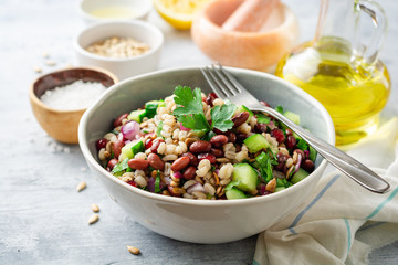 Healthy pearl barley salad with beans, cucumbers, red onion, sunflower seeds, pomegranate and parsley in bowl on concrete background. Selective focus.