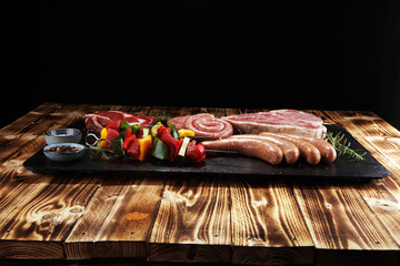 Assorted delicious raw meat with vegetable on a barbecue with t-bone steak, sausages and meat...