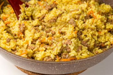 Frying pan full of yellow rice minced meat and wooden shovel