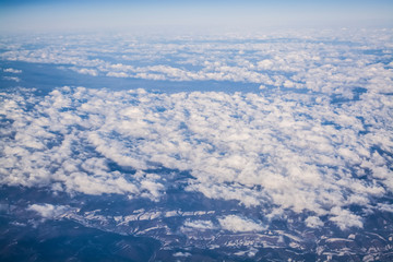 View from a plane window on clouds and blue clear sky and the earth from height. Beautiful view from air of mountains. 