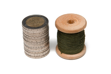Rows of coins isolated on white background next to multicolored thread on wooden spool