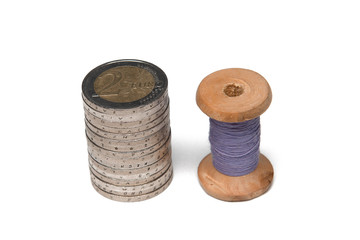 Rows of coins isolated on white background next to multicolored thread on wooden spool