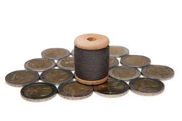 Rows of coins isolated on white background next to multicolored thread on wooden spool
