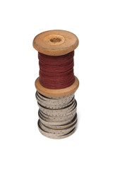 Rows of coins isolated on white background next to multicolored thread on wooden spool