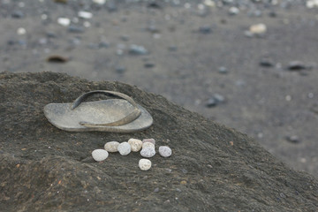 Fototapeta na wymiar A once-white thong and some pebbles sit on a black rock, abondoned playthings of a child.