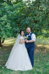 Newlyweds on their wedding day are walking in the park, looking at each other, smiling.