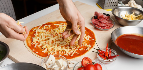 Chef sprinkling pizza with cheese at kitchen