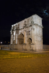 Fototapeta na wymiar arch of constantine of the roman forum viewed through the gated arch of the passage at the entrance of the Roman Colosseum at night.