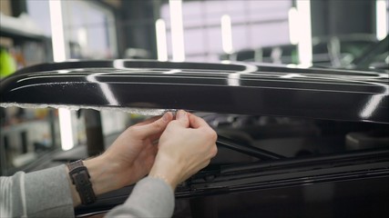 Workers remove the protective film from the machine.Deteyling car. Sticker protective film on the bumper of the car.