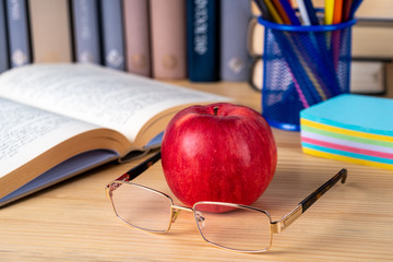 Back to school. Books, red apple, pencils and glasses on wooden table