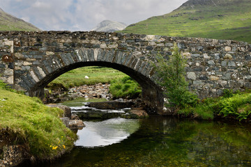 Fototapeta na wymiar Stone bridge over the Scarsdale river with sheep and peak of Ben More mountain in distance on Isle of Mull Inner Hebrides Highlands Scotland