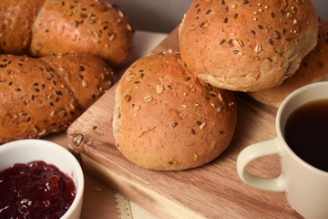 Whole grain bread and buns on the table with a cup of coffee and lingonberry jam. Close up breakfast food