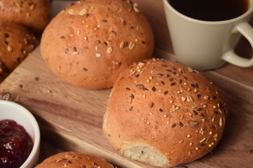 Whole grain bread and buns on the table with a cup of coffee and lingonberry jam. Close up breakfast food