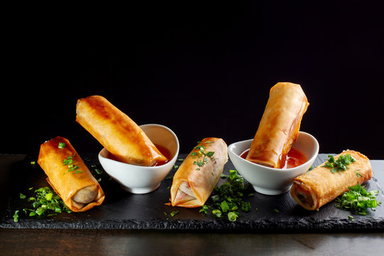Fried spring rolls on black slate decorated with greens.
