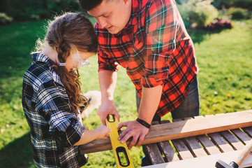 father teaching kid daughter to use tools. Girl helping dad with building work outdoor in summer, country house on background