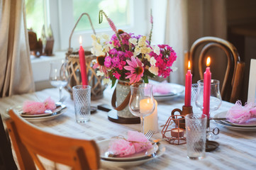 Obraz na płótnie Canvas summer festive table setting in beautiful country house. Table decorated with pink flowers and candles.
