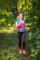 Fitness athlete woman running through park among trees on summer.