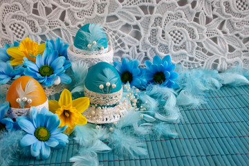Wielkanocne biało-błękitne tło z koronką, błękitnymi pisankimi , piórami, żółtymi i niebieskimi kwiatami © Monika