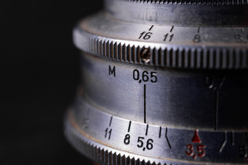 Vintage lens scales symbols closeup. Stock photo with blurred gray background. Aperture symbols and focusing distance sign on lens.