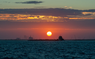 Fototapeta na wymiar golden sun setting over ocean with ocean vessel in foreground