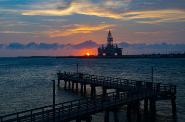 Fototapeta na wymiar Oil rig in construction in bay with setting sun behind it
