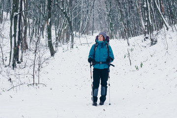 Fototapeta na wymiar Young girl with backpack looks aside hiking through the winter forest