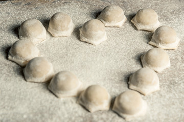 Fototapeta na wymiar Uzbek national food Chuchvara, like dumplings, lie in the shape of a heart, on a wooden board, in flour