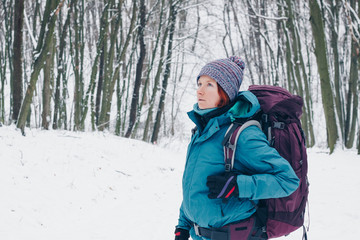 Fototapeta na wymiar Young girl with backpack looks up hiking through the winter forest. Look from the left side