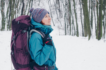 Fototapeta na wymiar Young girl with backpack looks up hiking through the winter forest. Look from the right side