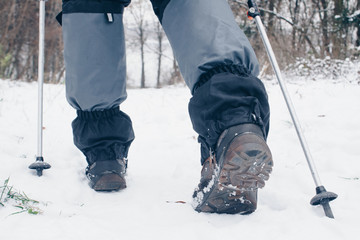 Hiker's boots with trekking poles and gaiters going backward in the winter forest
