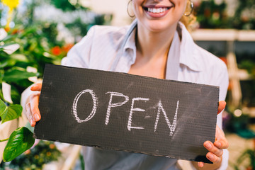 closeup of woman holding open sing . flower shop is open.